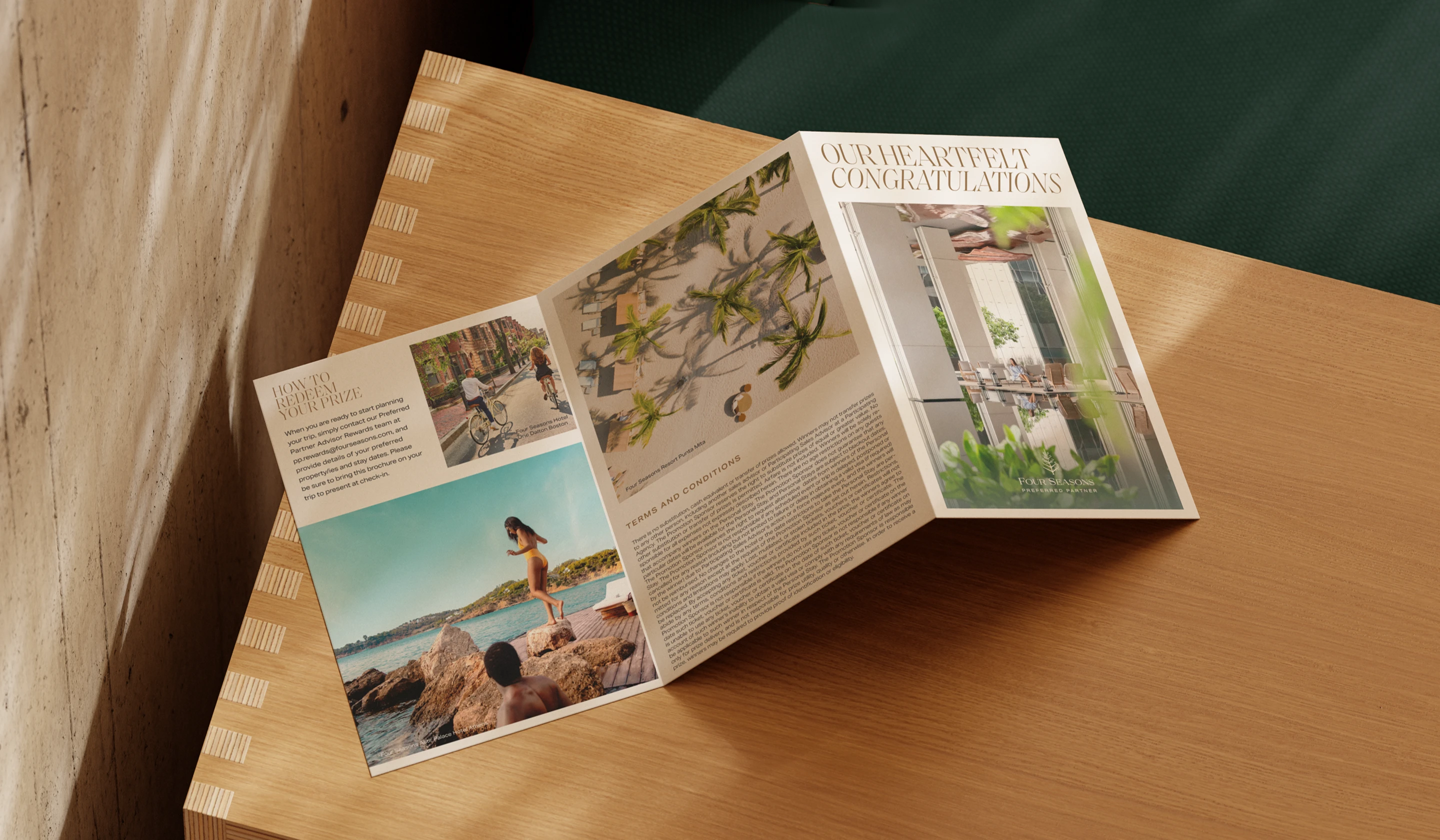 Fold-out Four Seasons brochure opened on a wooden table, showing interior spreads with photography, editorial text, and a cover reading ‘Our Heartfelt Congratulations.'