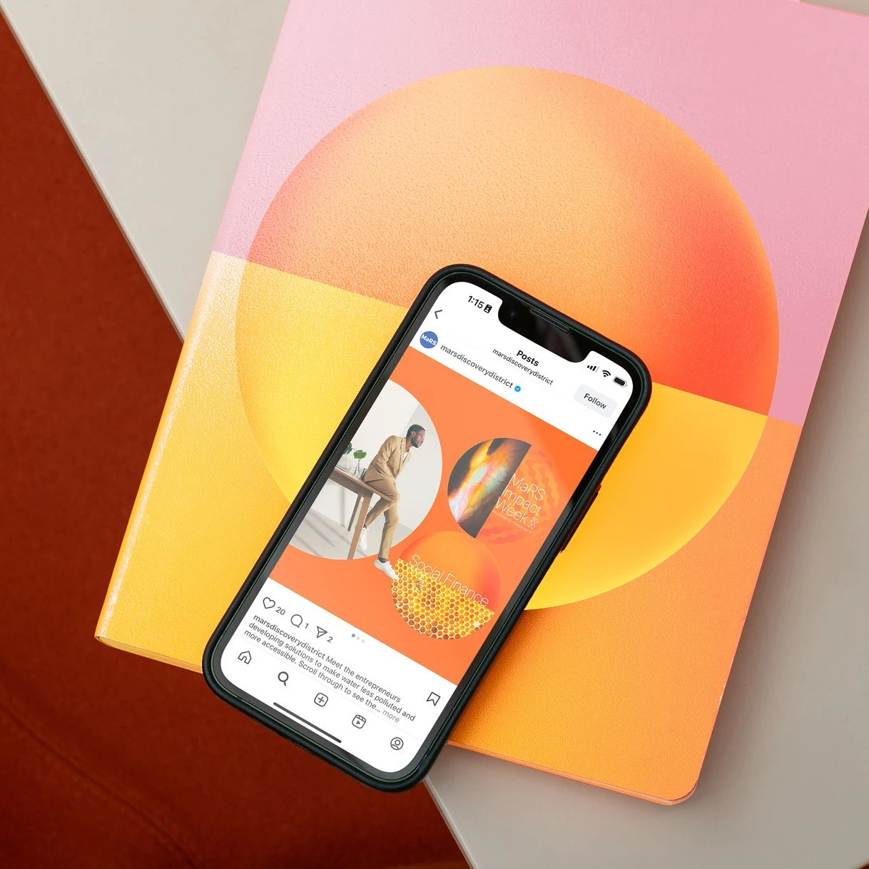 Phone showing a MaRS Instagram post resting on a printed booklet with gradient cover design
