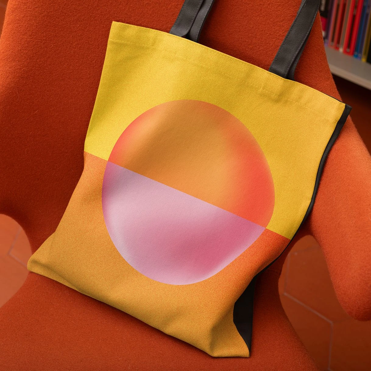Branded event tote bag with gradient circle graphic in orange and yellow tones, styled on a chair